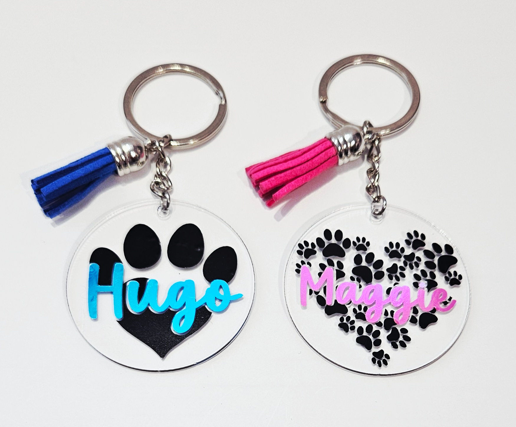 2 keychains, 1 with large pawprint and blue name & tassel and 1 paw print heart with pink name & tassel