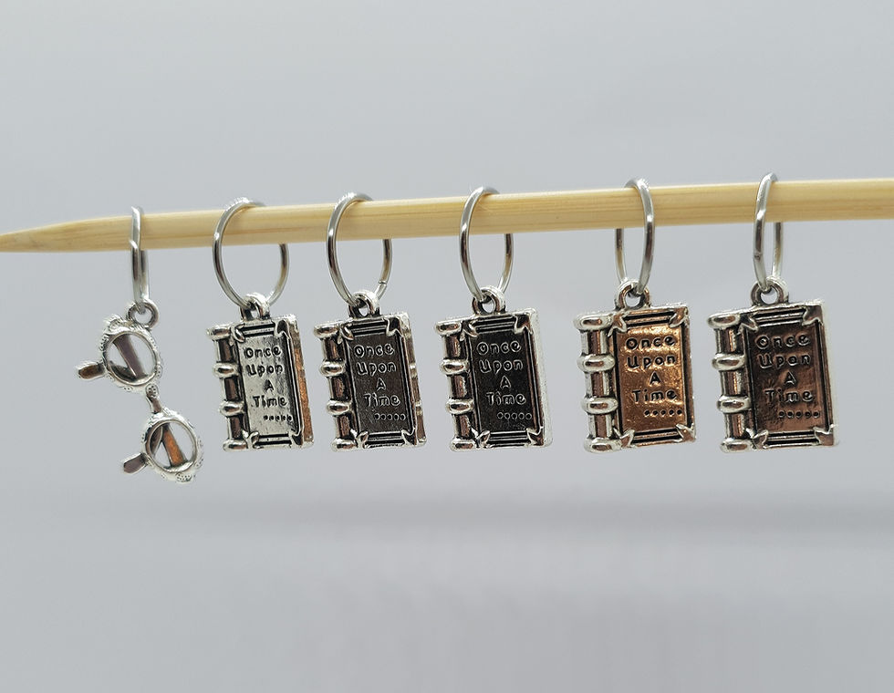 5 book charms and one pair of glasses charm on large rings on a knitting needle