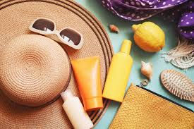 Straw hat, sunglasses, sunscreen, and a lemon on a turquoise background. Purple scarf with white dots adds a summery, relaxed mood.