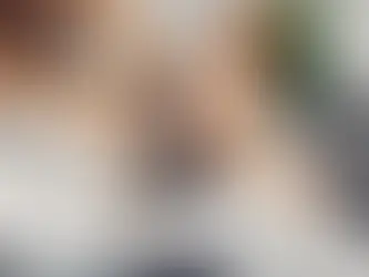 Woman getting hair washed at a salon, smiling and relaxed. Hands apply shampoo in modern sink, with bottles in the blurred background.