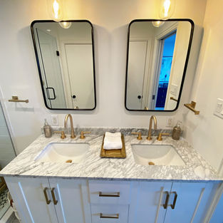 legant white double vanity with marble countertop, gold hardware, and modern mirrors.