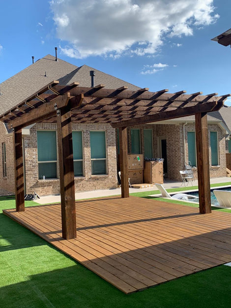 Wooden pergola installed over synthetic green turf in a backyard.