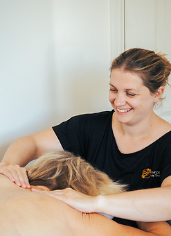 Image shows a smiling Beth massaging a female's traps and shoulders
