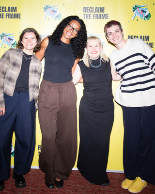 Four women standing and smiling in front of a yellow “Reclaim the Frame” backdrop at a film screening