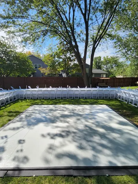 a white dance floor in a backyard with tables and chairs