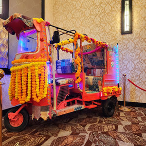 A brightly colored pink and orange auto-rickshaw decorated with yellow marigold garlands and blue LED lights, parked indoors 