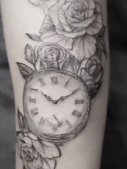 Image of a forearm with a fine line clock and roses tattoo