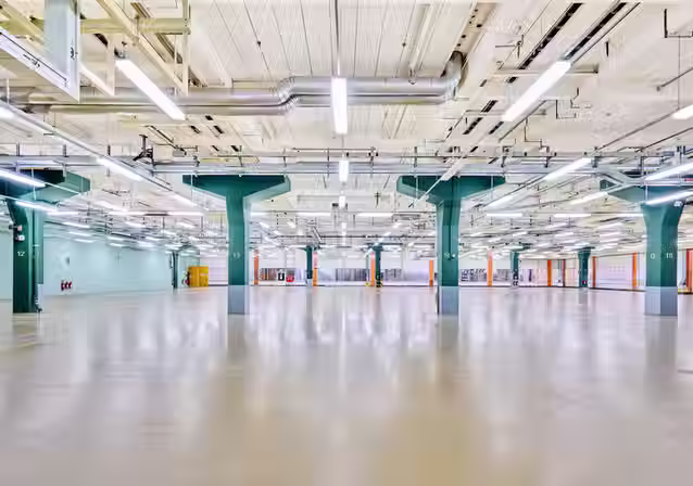 Große, leere Veranstaltungshalle NLND Bay 5 in Berlin mit hellen Böden und markanten grünen Stahlbeton-Pfeilern.