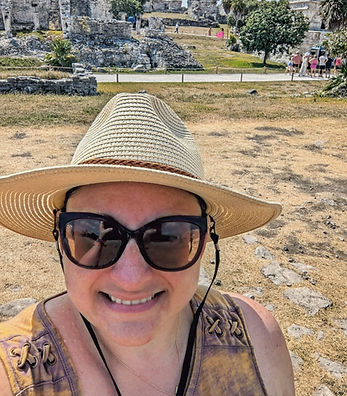 Smiling woman wearing a straw hat and sunglasses standing in front of Mayan ruins