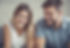 A close-up portrait of a young man and woman laughing together while looking down at something off-camera.