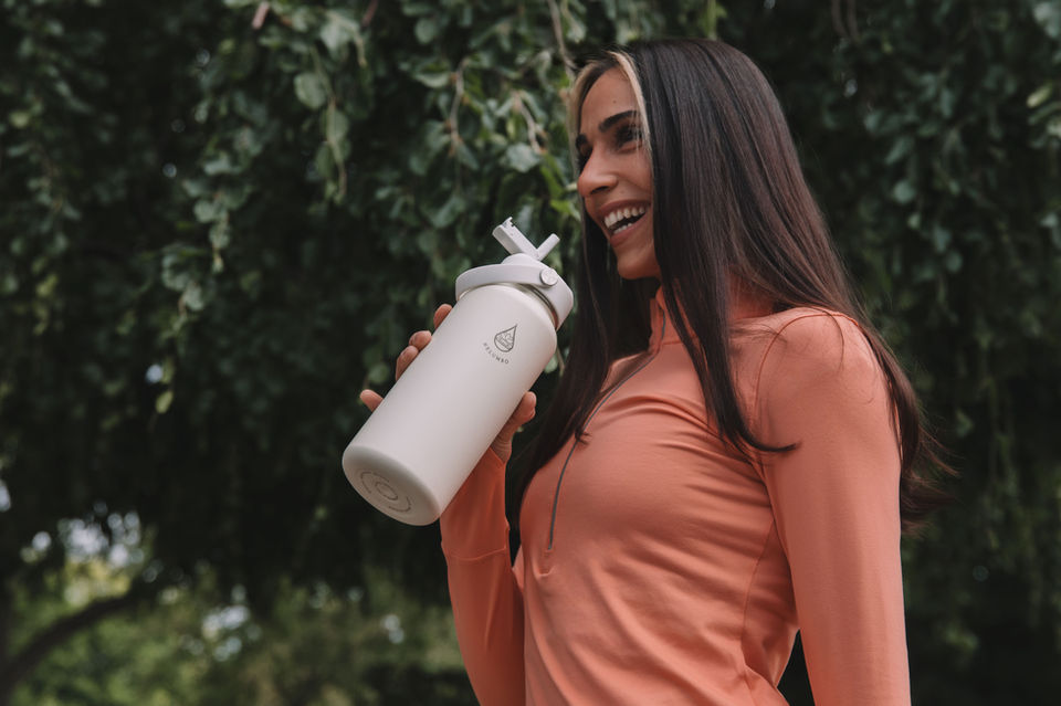 Smiling woman drinks from a white water bottle; enjoying the refreshing drink.