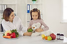 Doctor teaching child to eat fresh healthy food. Dietitian or nutritionist talking to litt