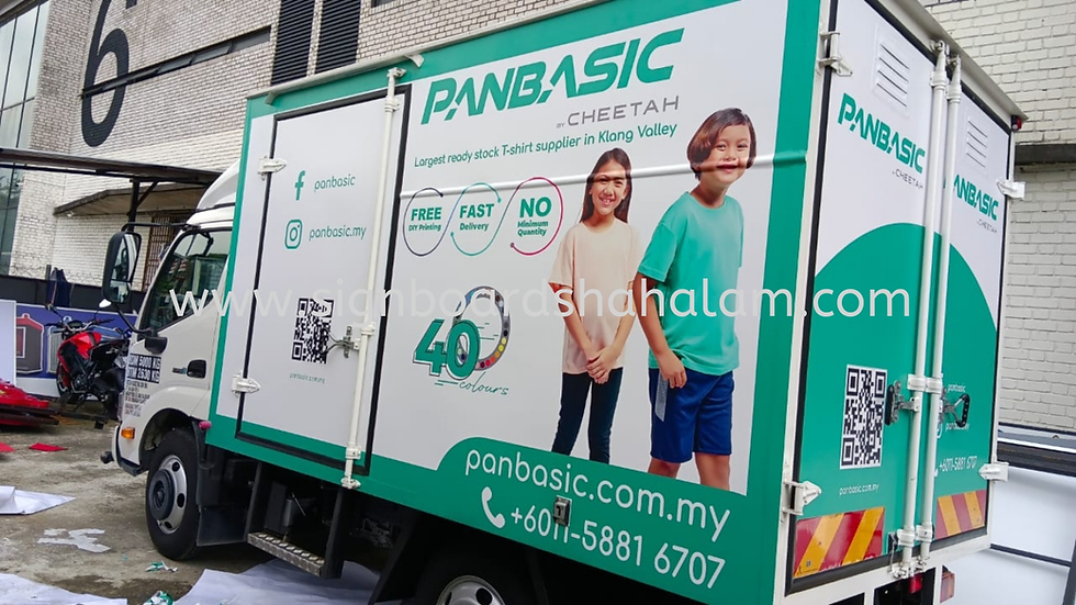 Lori putih dengan branding "PANBASIC", gambar kanak-kanak tersenyum & maklumat perkhidmatan. Latar bandar.







