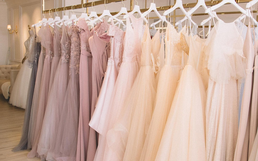 Elegant pastel gowns on hangers in a boutique, showcasing embroidery and lace details. Soft lighting and classic decor create a luxurious feel.