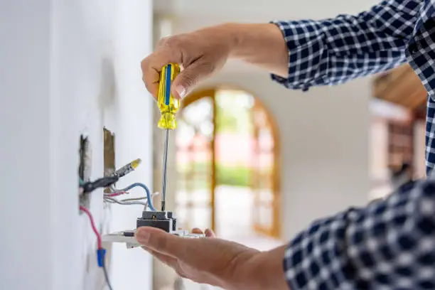 Teknisi profesional sedang menyemak sambungan wiring rumah dengan pemutar skru.