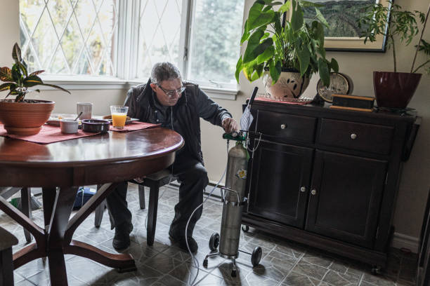 Man adjusting oxygen tank in a cozy room with plants and wooden furniture. Daylight filters through the window. Table set with breakfast items.