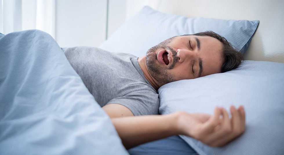Man with sleep apnea sleeping on blue-striped bedding, wearing a gray shirt, mouth open. Background is blurred, conveying a peaceful, restful mood.