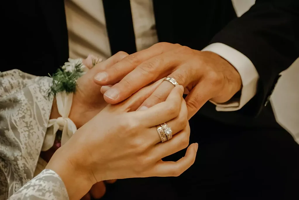 Hands of a couple with wedding rings, tenderly holding each other. One wears a floral wrist corsage. Scene conveys love and unity.
