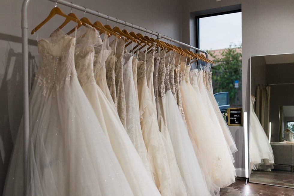 Elegant wedding dresses hang on a rack in a boutique, reflected in a mirror. Bright, neutral tones with a calm, inviting atmosphere.