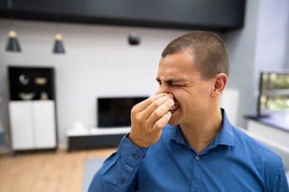 a man is covering his nose and closing his eyes, showing that he is not comfortable with aircond smell