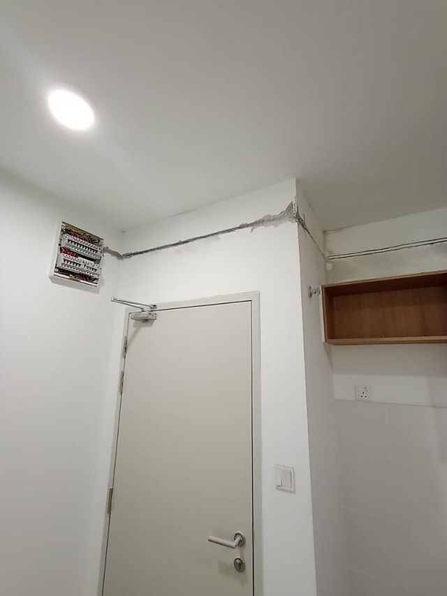 Pemandangan dalaman bilik putih dengan kotak agihan elektrik terletak di atas pintu, menampilkan wiring permukaan yang kelihatan.
