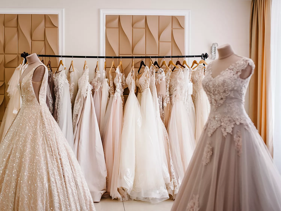 Elegant wedding dresses on hangers and mannequins in a boutique, featuring lace and sequin details. Beige walls and soft lighting enhance elegance.