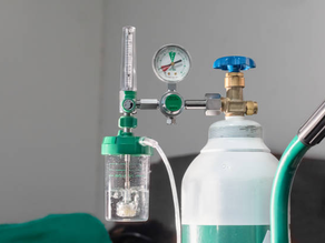 Oxygen tank rental with pressure gauge and green valve in a clinical setting. A tube is connected with clear water inside a flow meter.