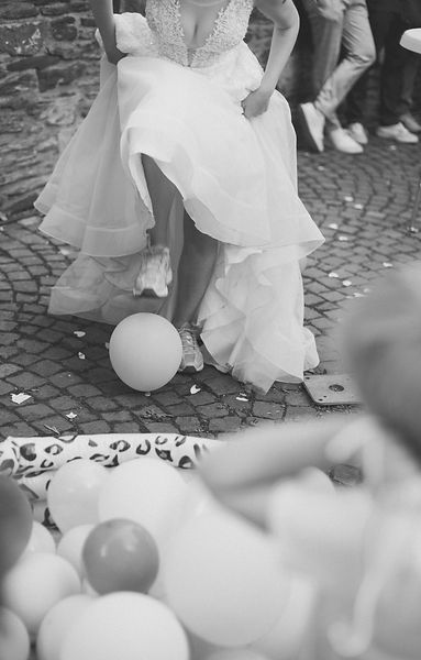 Ungezwungener Moment bei Hochzeitsspiel – Braut mit Turnschuhen lacht beim Luftballon-Spiel auf der Feier