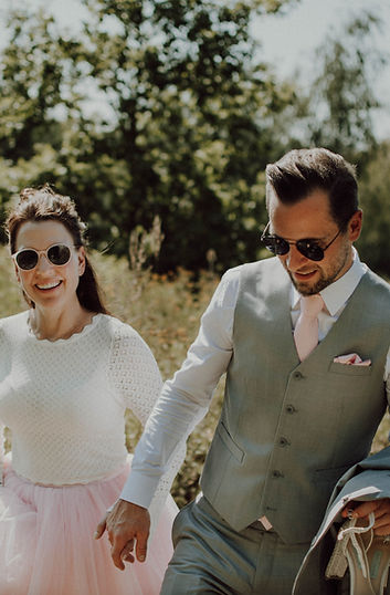 Hochzeitspaar mit Sonnenbrillen schlendert Hand in Hand durch eine Sommerwiese in Wiesbaden – entspannte Hochzeitsreportage