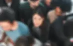A young woman surrounded by people looks anxious, showing visible signs of psychological distress.