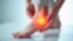 Person experiencing heel pain holds their injured foot, indicating possible plantar fasciitis or other foot injury.