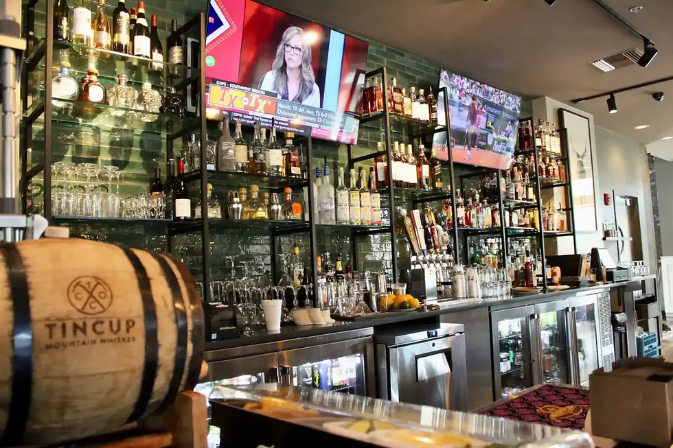A bar with wall to wall alcohol and some HD TVs with sports on them.