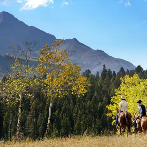Three people horseback riding through mountains.