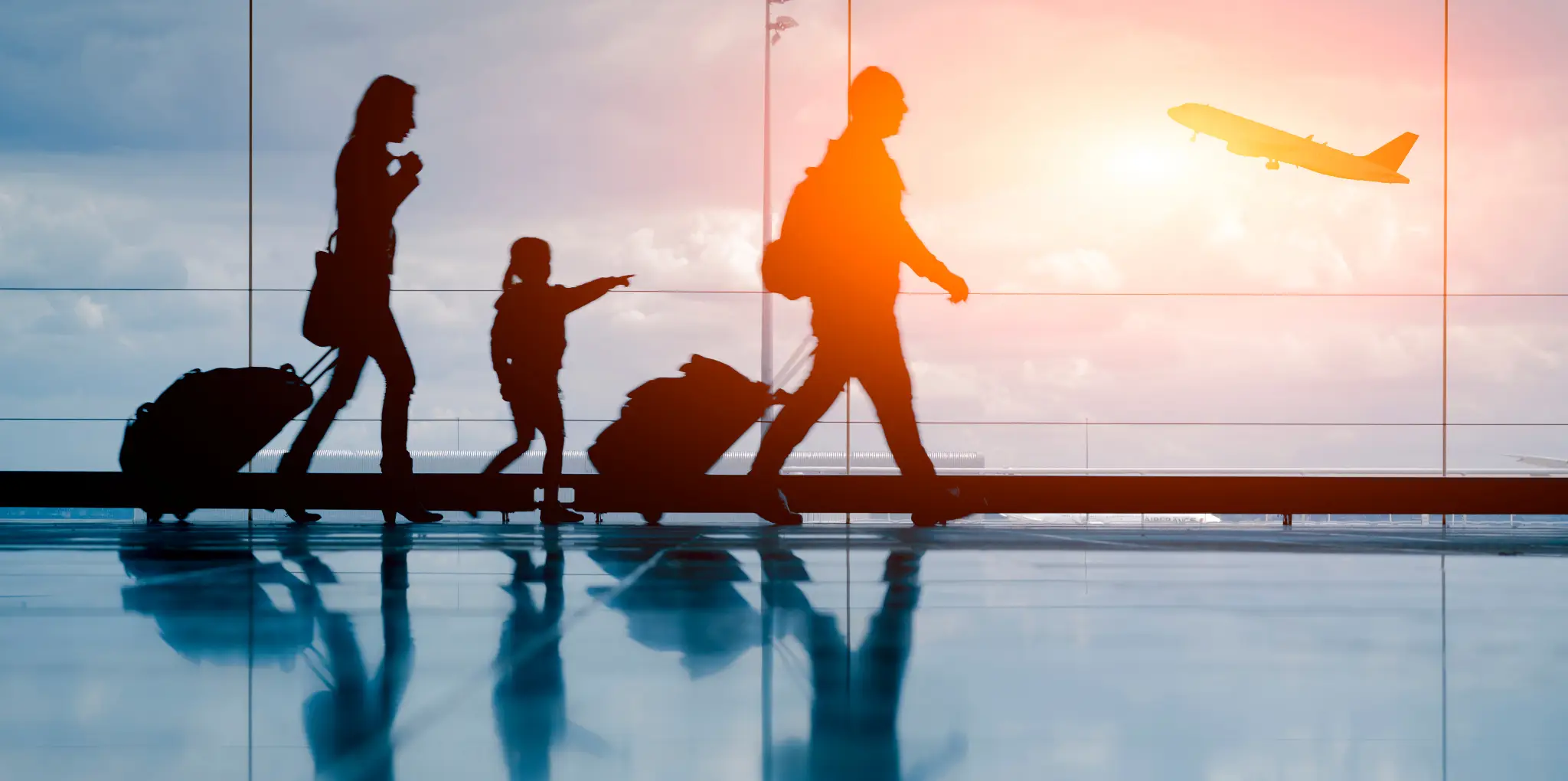 A silhouette of a family walking at the airport while a plane is taking off.