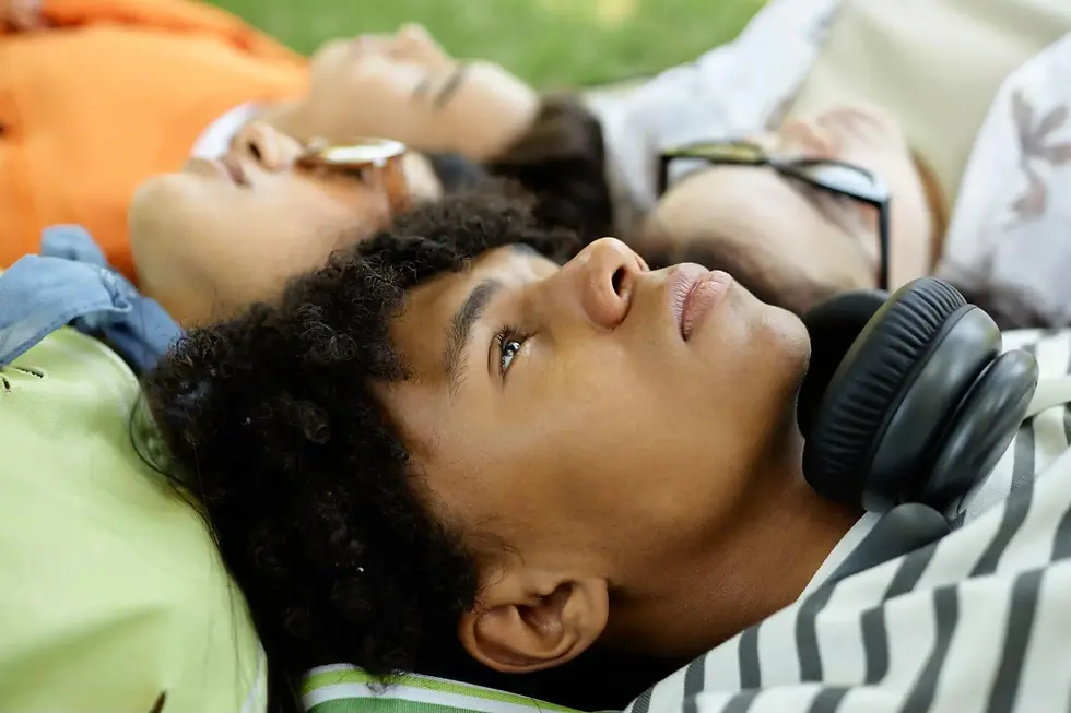 A boy lying on the grass with friends in the park stares blankly at the sky.