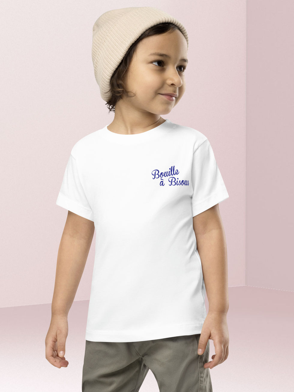 Adorable jeune garçon posant en tee-shirt blanc imprimé bouille à bisous et un bonnet beige sur la tête