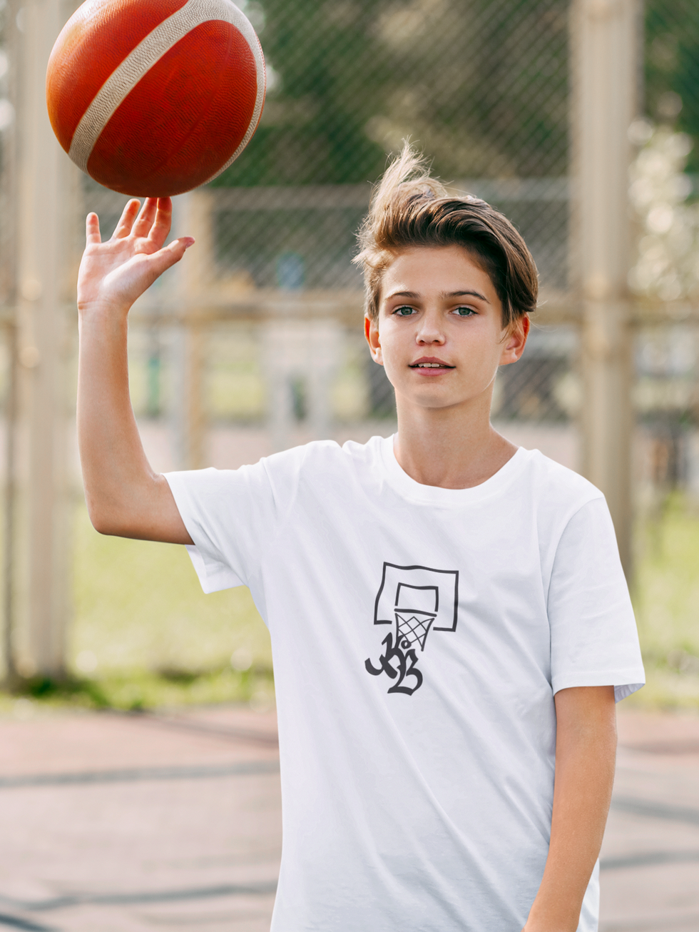 garçon blond qui porte un tee-shirt blanc imprimé du sigle en noir de Krew of Ballers sous un panier de basket