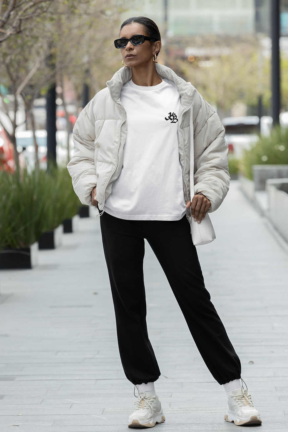 femme dans la rue qui porte un jogger pant noir brodé krew Of Ballers avec un sweatshirt blanc et une doudoune courte crème