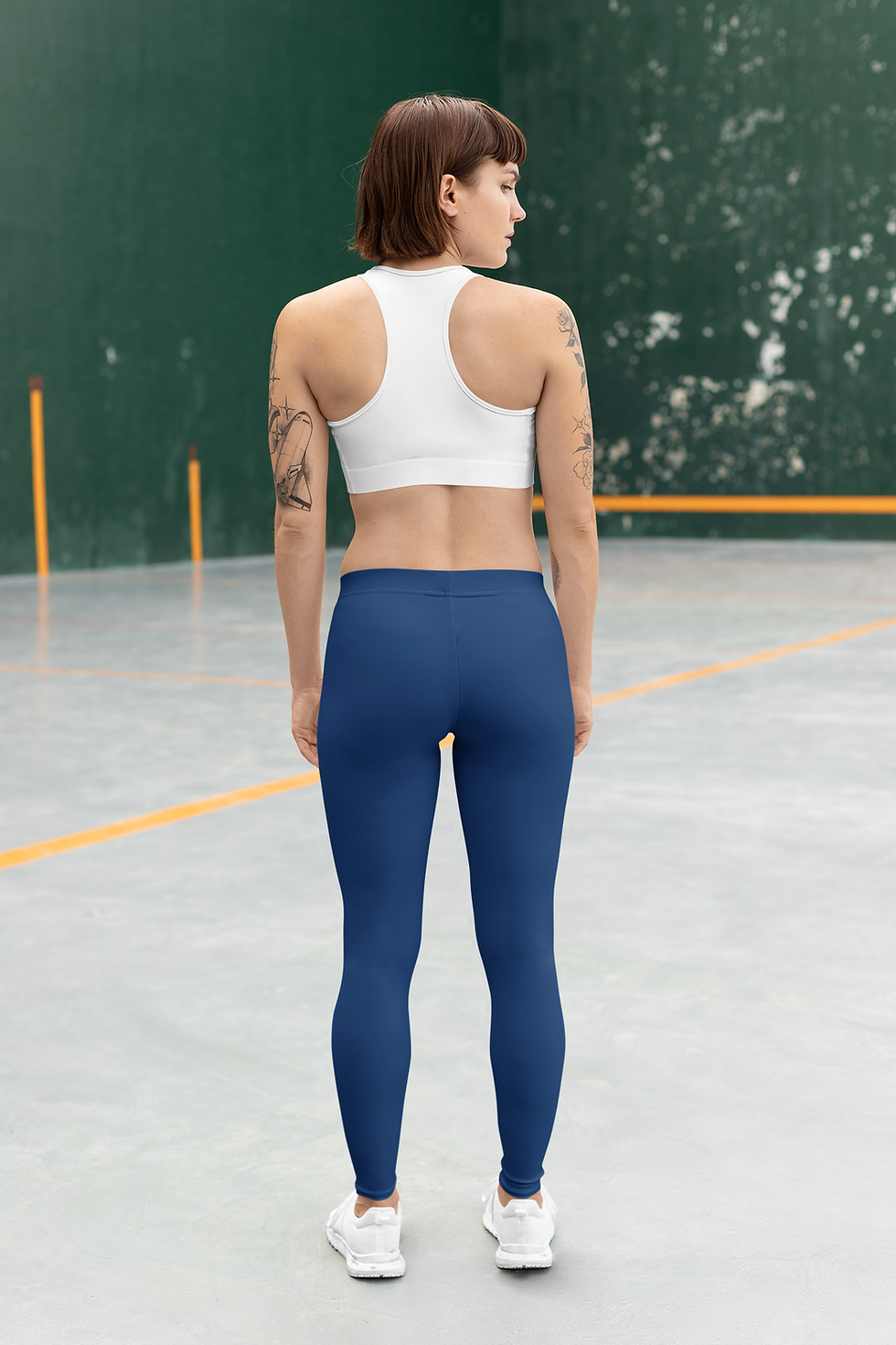 back view of an attractive woman on a tennis court wearing a white racer back sport bra and blue leggings