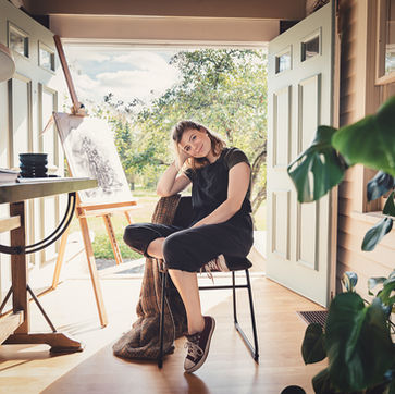 Woman sitting in studio with a painting, smiling at the viewer.