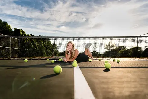 Young woman lies on tennis court surrounded by tennis balls, net. About Sharmila Taylor Phot