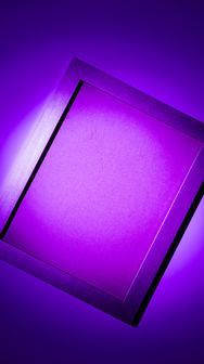 A rectangular purple neon light frame glowing against a dark studio wall. Credit goes to "Moments By Migs".
