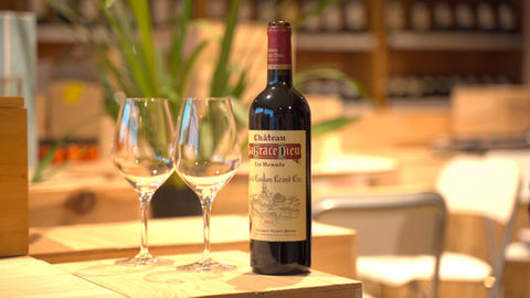 Bouteille de vin rouge de Saint-Emilion Grand Cru, le Château La Grâce Dieu, avec deux verres à vins de dégustation, avec en fond des étagères de vins.