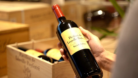 bouteille vin rouge de Saint-Julien Pavillon de Léoville Poyferré 2015 tenue dans la main avec en fond sa caisse en bois contenant cinq bouteilles.