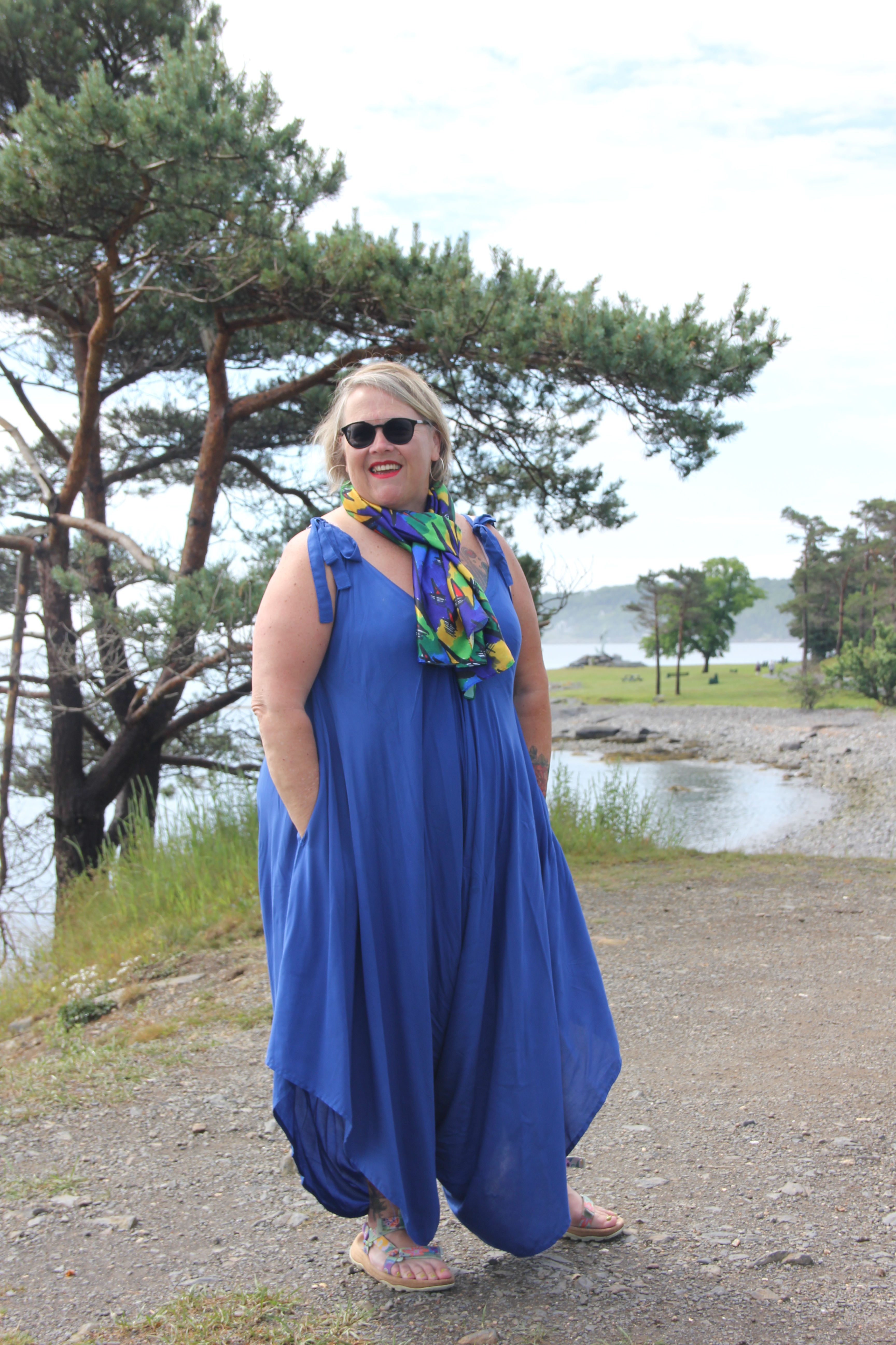 Smiling woman in blue dress and scarf by rocky shore