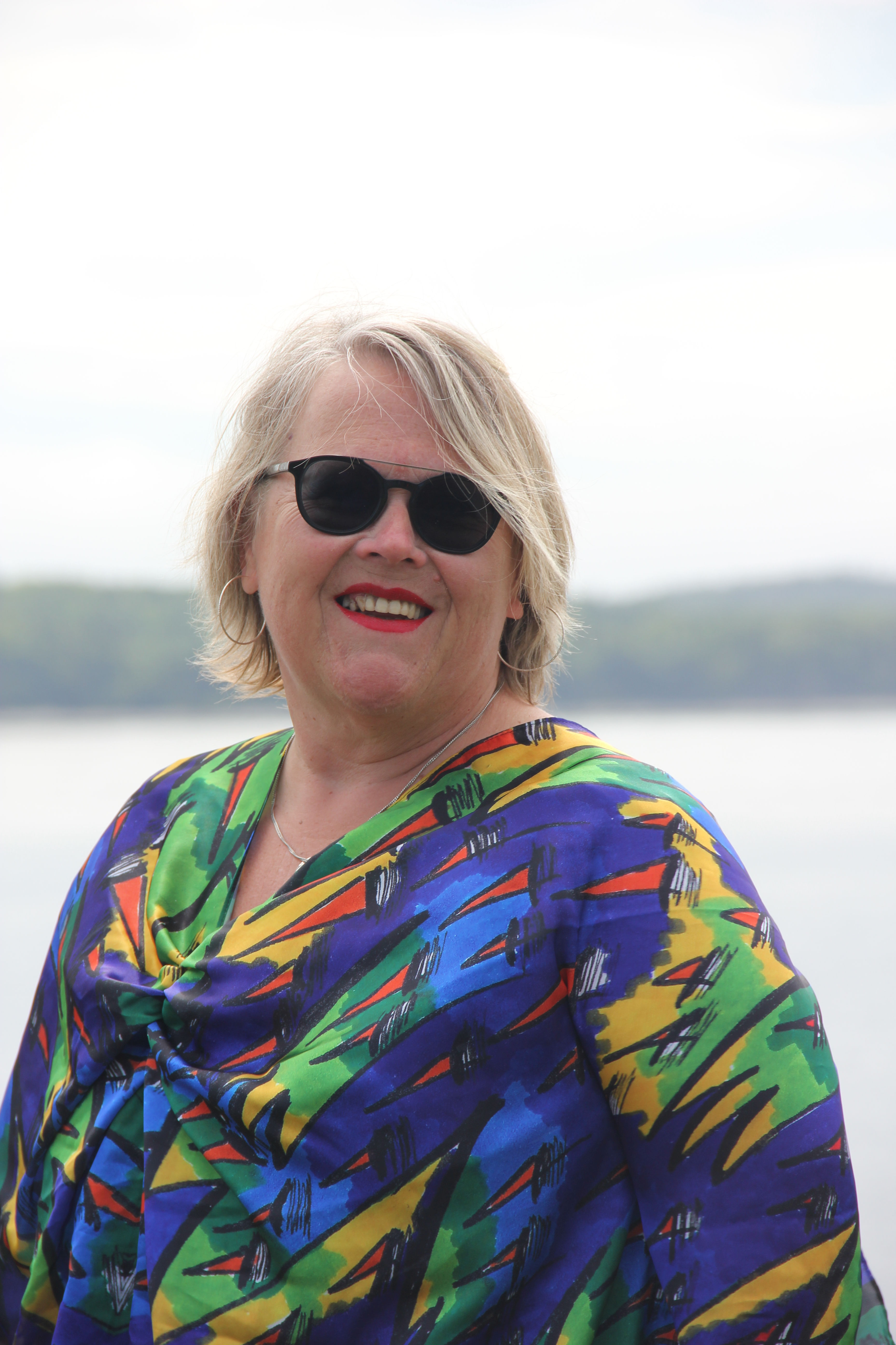 Smiling woman with short blonde hair, sunglasses, colorful top
