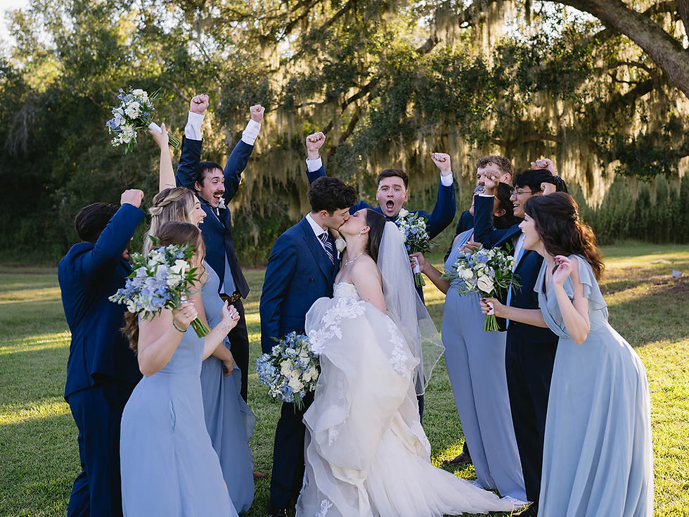 Wedding party cheering as bride and groom kiss under oak trees.
