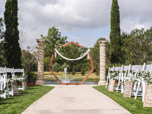 Outdoor wedding altar with wooden hexagon arch by a fountain.
