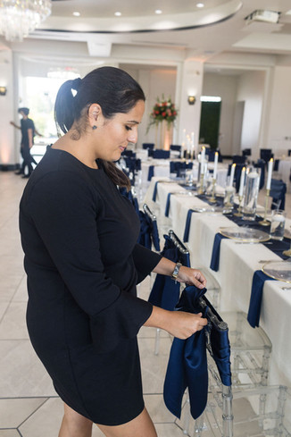 Wedding planner adjusting navy chair sashes in elegant reception space.