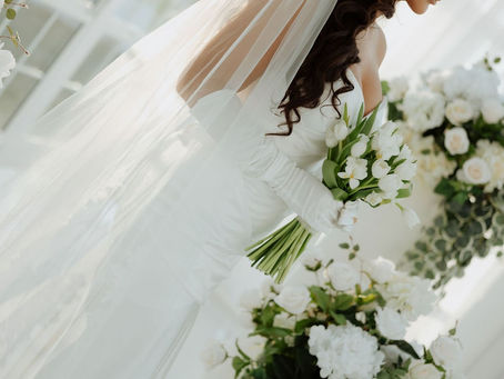 Bride in white dress with tulip bouquet, surrounded by flowers, veil flowing in soft light